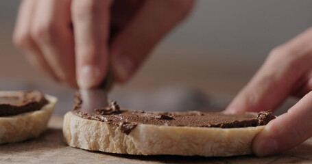 man spreading chocolate nut spread on ciabatta slice on olive board
