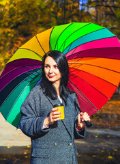 Young happy woman in a coat under an umbrella. Young girl with long black hair with an umbrella in...