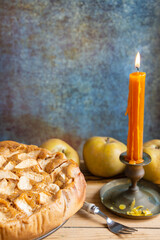 Top view of apple pie on wooden table with pippin apples, fork and candle, selective focus, gray background, vertical