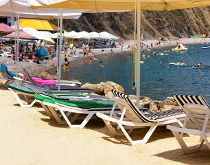 Beach by the sea. Sun loungers and sun awnings. Sand, water, tourists. Photo.