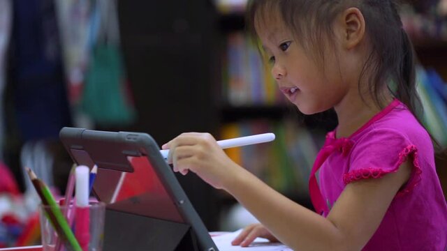 Online education concept. Online class. Asian little girl studying at home. kid in living room at home and using digital tablet to draw.
