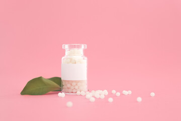 Close-up image of homeopathic globules in glass bottle on pastel pink background. Homeopathy...