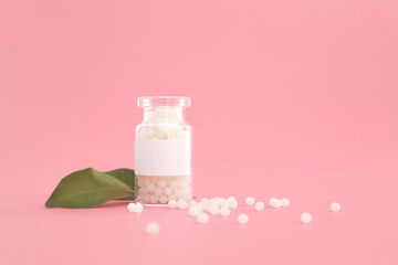 Close-up image of homeopathic globules in glass bottle on pastel pink background. Homeopathy pharmacy, herbal, natural medicine, alternative homeopathy medicine, healthcare. Free space, copy space.