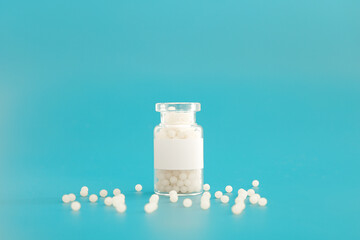 Close-up image of homeopathic globules in glass bottle on blue background. Homeopathy pharmacy,...
