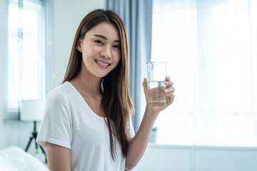 Portrait of Asian attractive woman holding a glass of water in bedroom.