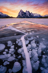 Stunning sunrise with leading ice creacked line and trapped frozen methane bubbles within ice surface, Lake Abraham, Alberta. Winter storm in Canada. - obrazy, fototapety, plakaty