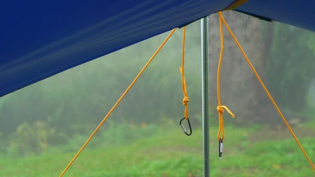wind blowing and rain drops on blue tent and tarp with tent accessory rope with carabiner.