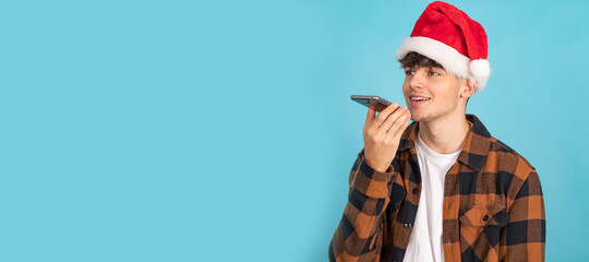 young man in santa claus hat sending voice message isolated on blue background