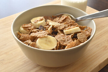 Fototapeta na wymiar Fruit and fiber cereal with banana and milk with a spoon in a bowl on a bamboo chopping board. 