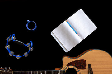 Acoustic guitar, tambourine, notepad and coffee cup on black background.