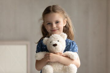 Portrait of smiling adorable preschool small kid girl cuddling favorite fluffy toy, posing alone at home. Happy cute 7s little child daughter holding teddy bear, feeling cheerful in kindergarten.