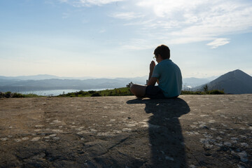 blond boy sitting on a rock on the mountain, meditating with his hands together.