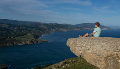 boy sitting on a rock high above watching the sea