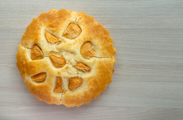 Freshly baked homemade apple pie charlotte cracked with golden crust and dough cracks and apples on a light wooden background. The light falls on the pie, flat lay, closeup, copyspace.