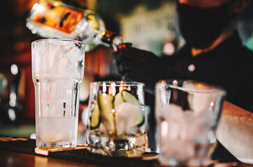 hands of a bartender with black gloves making cocktail on a bar counter.