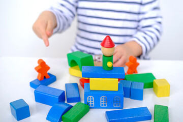 kid, small child, 2-year-old girl builds towers and buildings from colored wooden figures, concept of housing construction, mortgage, insurance, happy childhood, children's games