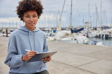 Horizontal shot of good looking creative woman draws creative image on touchpad wears blue...