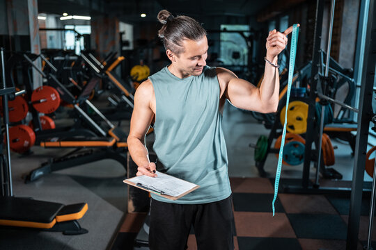 young handsome personal trainer nutritionist with measuring tape in gym - Powered by Adobe