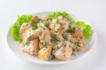 Baked potatoes in sour cream sauce with herbs are placed in a white plate on lettuce leaves. Close-up