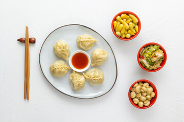 Boiled dumplings or wonton dough stuffed with minced meat in a plate with sauce on a white table along with chopsticks, pickled mushrooms, hot peppers and cabbage salad. Homemade food. Top view