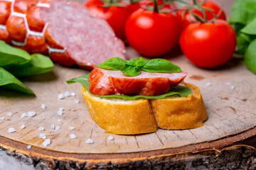 Simple sausage sandwich on cutting board, vegetables and ingredients from behind