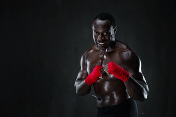 African american athletic fighter demonstrating boxing stance, raising fists up, black background,...