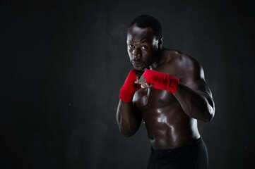 Athletic boxer during boxing training. Fitness african american muscular model over black background. Strength, fighting and motion project.