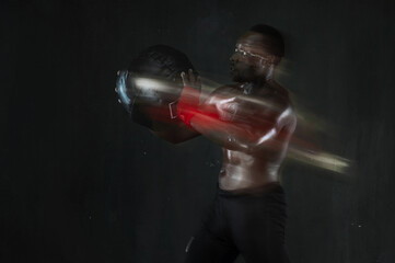 Fototapeta na wymiar Shot of muscular man doing functional training workout with wall ball. African american fitness male working out with a medicine ball on black background. Long exposure. Copy space.