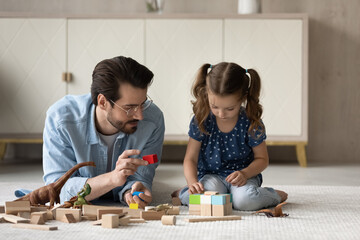 Joyful young father and little cute kid daughter playing wooden toys in modern living room, happy...