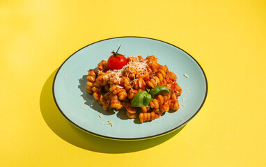 Creative flat lay background with Pasta, tomato sauce, cheese and basil on a blue plate. Yellow backdrop.