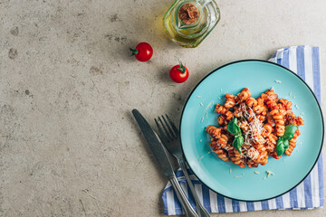 Tomato pasta with cheese on blue plate with napkin and cutlery on a stone background. Minimal flat lay.