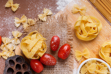 Yummy italian pasta and cherry tomatoes in rustic style on brown background. Traditional italian cuisine top view. Pasta is the traditional italian food. Spaghetti, fettuccine, farfalle flat lay view.