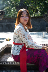 Young Local Girl at posing with a traditional gold sarong in front of a temple in Bali island, Indonesia