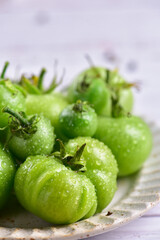 Green tomatoes with water drop on a white plate, close-up.