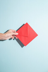 Hand holds an envelope on a blue background. Hard shadows