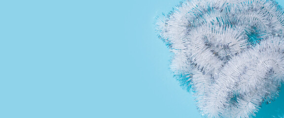 White fluffy Christmas New Year tinsel on a blue background. Top view, flat lay. Banner