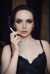 Lovely beautiful young woman in lingerie smoking cigarette. Portrait of beautiful girl in black bra