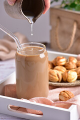 Milk from the milkman is poured into a glass with coffee, in the background nuts with condensed milk.