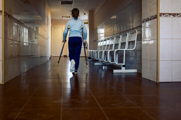 Child walks along hospital corridor on crutches to see doctor. Girl has one leg broken in cast.