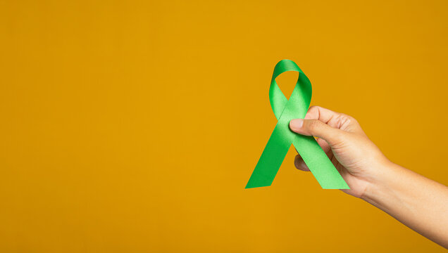September world lymphoma awareness day and October world mental health day. Hand holding of a green ribbon over on a yellow background. Healthcare and medicine concept