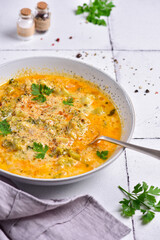 A plate of cheese soup, with parsley, on a white stone tile, next to a gray napkin, side view.