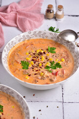 Tomato soup with parsley and corn, on a white stone tile, side view.