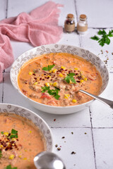 Two plates of tomato soup, parsley, and corn, on a white stone tile, side view.