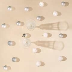champagne glasses on a beige table with interesting shadows.Christmas baubles all around in white and silver color.sparkly holiday party flat lay concept