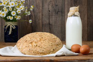 Homemade bread, eggs, milk and bouquet of daisies on rustic wooden table