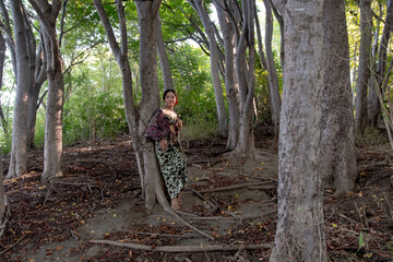 Naklejka na ściany i meble Balinese girl posing in nature and in a forest on Candidasa's offshore islands in Bali, dressed in a traditional costume. 