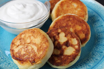 cheesecakes curd pancakes lie on a blue plate dish near sour cream. breakfast cottage cheese homemade breakfast