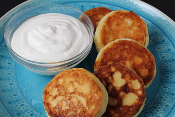 cheesecakes curd pancakes lie on a blue plate dish near sour cream. breakfast cottage cheese homemade breakfast