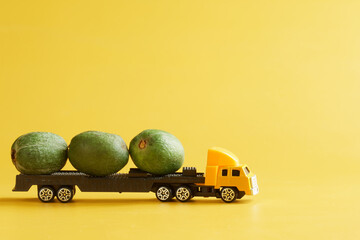 A toy truck carrying fresh feijoa. Yellow background. Delivery concept for large-sized items and...