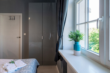 Contemporary interior of bedroom in grey colors. Modern apartment. Flower on sill. White door. Wardrobe.